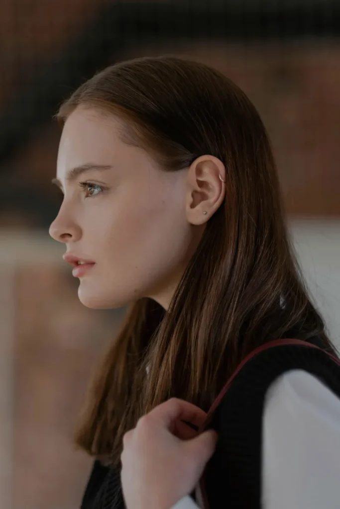 Profile view of a woman with sleek, pin-straight long hairstyles for the quiet luxury aesthetic, with her hair tucked neatly behind her ear to highlight minimal jewelry.