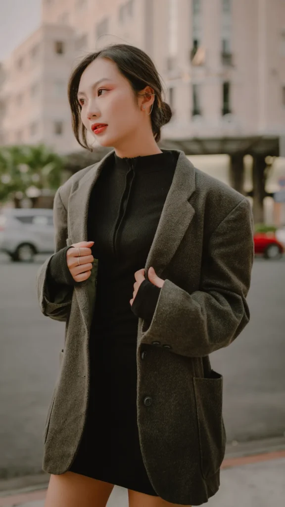 A young woman outdoors wearing a structured, charcoal grey tailored blazer over a black high-neck top, demonstrating an impeccable fit that exemplifies the "Old Money" French aesthetic and 2026 fashion trends.