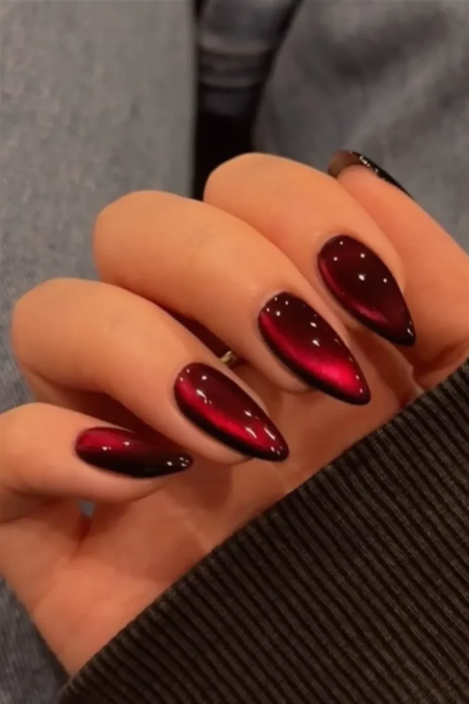 Close-up of a hand showcasing a high-end, almond-shaped manicure with a striking velvet cat-eye effect. The nails feature a glossy, ultra-dimensional magnetic polish that shifts from a deep, velvety black around the edges to a rich, glowing crimson red in the center, mimicking a shimmering gemstone or silk texture.