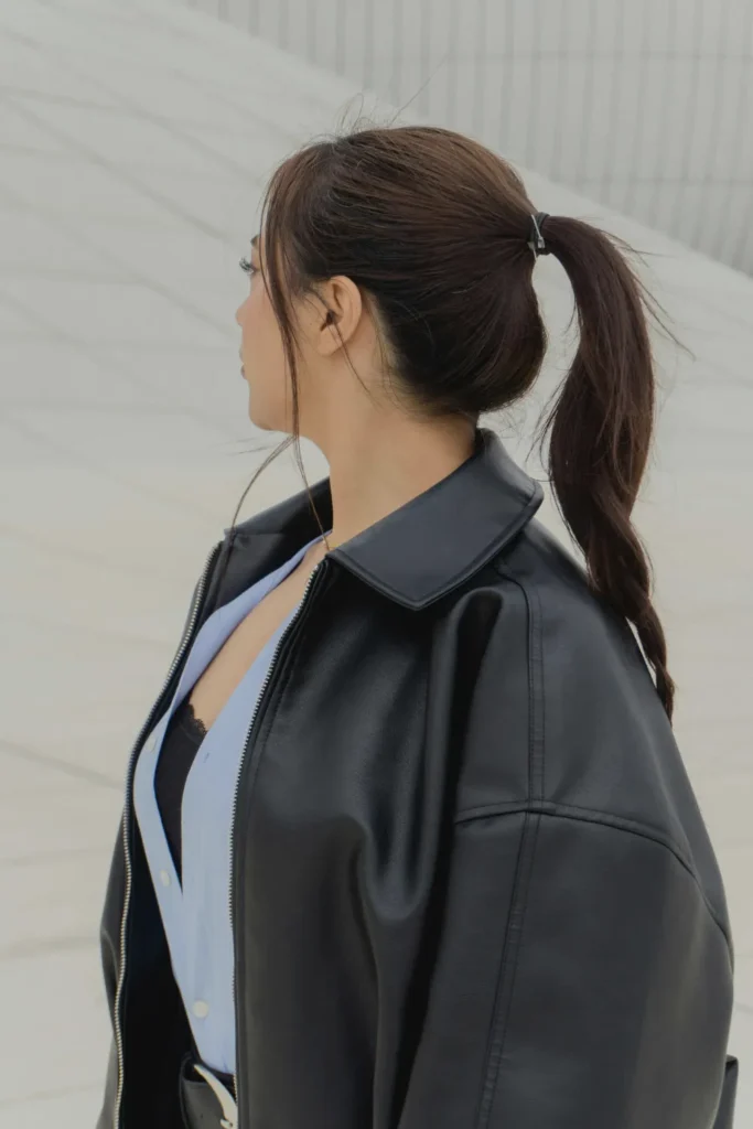 Side profile of a woman wearing a voluminous crown ponytail, showcasing sophisticated long hairstyles for the quiet luxury aesthetic paired with an oversized black leather jacket.