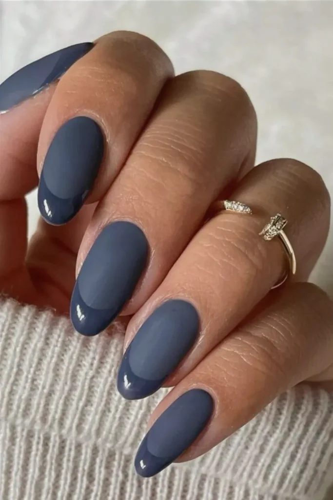 Close-up of a hand showcasing a sophisticated, medium-length oval manicure featuring a monochromatic navy blue color palette. The nails demonstrate a stylish texture contrast with a smooth, matte finish applied to the main nail beds, paired with a matching, ultra-glossy French tip in the exact same deep slate blue shade.